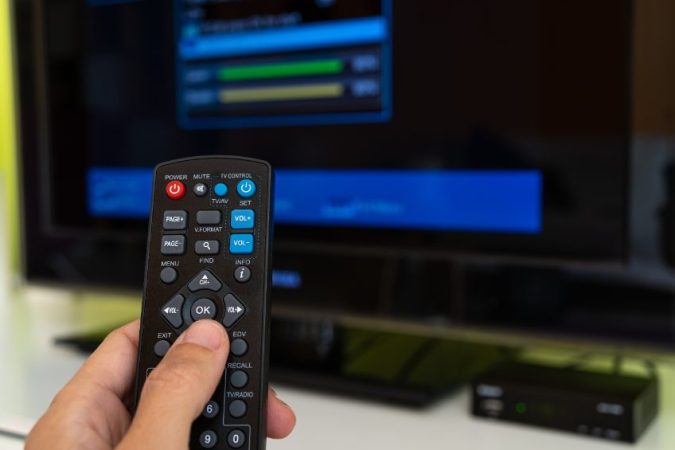 Personne utilisant une télécommande pour naviguer sur l'interface d'une application IPTV fiable affichée sur un écran plat