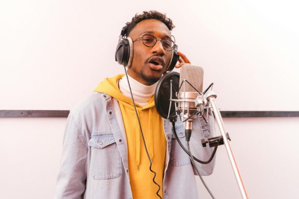 Un jeune chanteur avec des lunettes et un casque audio enregistre un morceau devant un microphone de studio professionnel.
