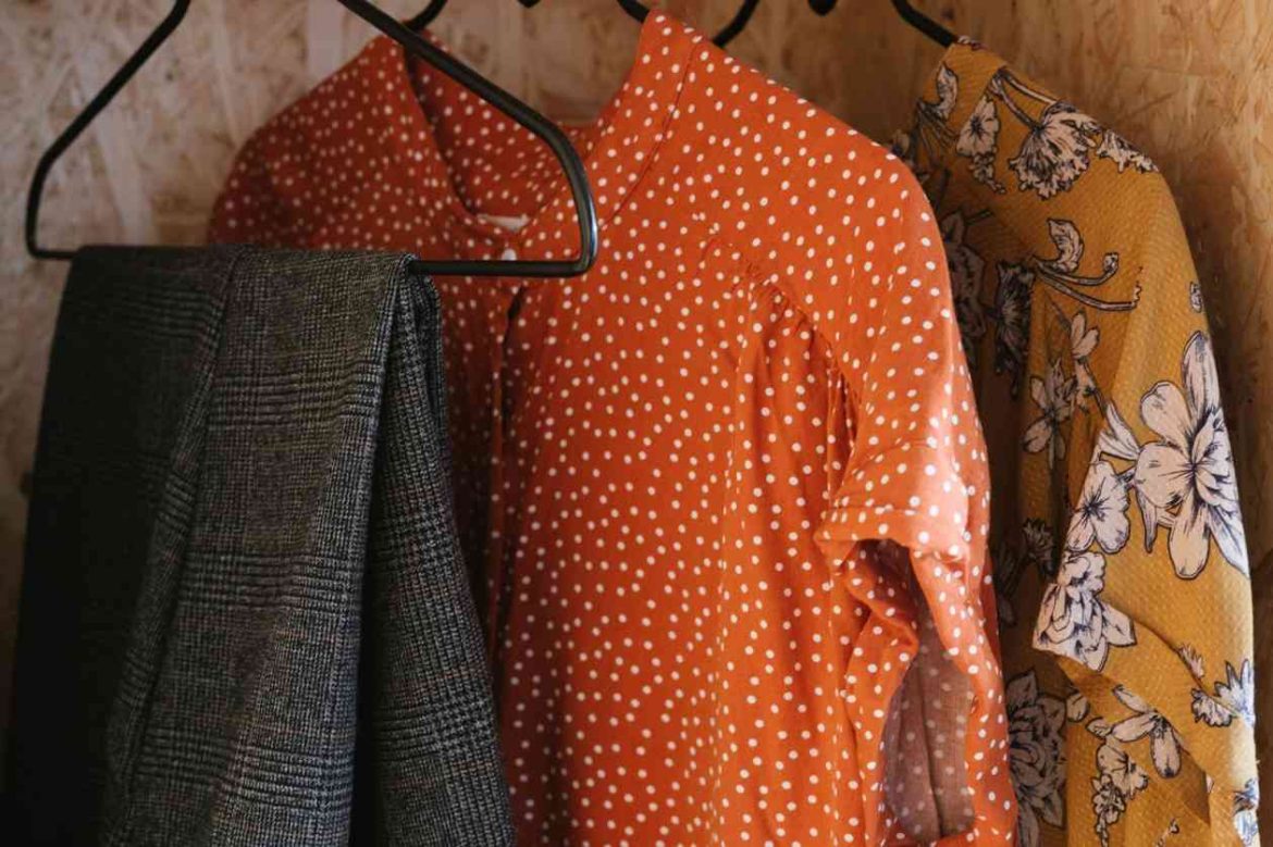 Des vêtements colorés suspendus sur des cintres fins en métal noir dans une penderie, illustrant comment déménager ses vêtements sur cintres sans les froisser.